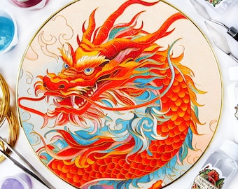 May include: A round, white plate with a gold rim features a detailed illustration of a red dragon with blue and yellow accents. The dragon is surrounded by clouds and waves. The plate is surrounded by various craft supplies, including paint bottles, a palette knife, and a bottle of temporary fixing glue.