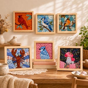 Peut inclure: Six pièces d'art textile encadrées de forme carrée présentant des motifs matelassés d'un cardinal rouge, d'un geai bleu, d'un petit oiseau, d'un homard, d'une tête de geai bleu et de champignons, le tout dans des cadres en bois clair.