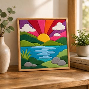 Op de afbeelding: Een vierkant ingelijst kunstwerk met een vilten landschap met een gele zon, levendige veelkleurige stralen, witte wolken, groene heuvels, een blauw meer en grijze rotsen, geplaatst in een lijst van lichtgekleurd hout.