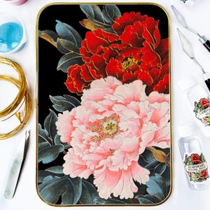 Pode incluir: Uma impressão de arte retangular com moldura dourada apresenta um design floral de peónias vermelhas e rosas sobre um fundo preto. As flores têm detalhes dourados e são rodeadas por folhas verde-escuras. Materiais de artesanato, incluindo cola e ferramentas, são visíveis.