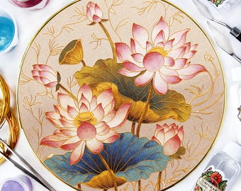 Può includere: Piatto decorativo rotondo con un'illustrazione dettagliata di fiori di loto. I fiori sono rosa e bianchi con centri gialli, su uno sfondo beige con accenti dorati. Il piatto ha un bordo dorato e foglie blu e verdi.