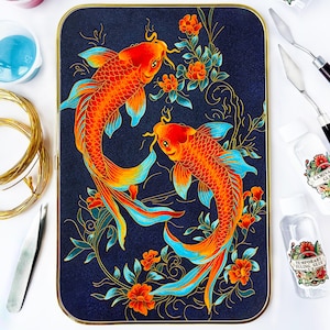 Puede incluir: Una bandeja decorativa con dos peces koi de color naranja y rojo con aletas azules, rodeados de flores naranjas y follaje verde, sobre un fondo azul oscuro. La bandeja tiene un borde dorado.