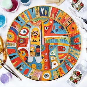 Pode incluir: Um prato decorativo com um design abstrato em cores brilhantes, incluindo vermelho, azul e amarelo, com uma borda e uma borda de corda dourada. O prato é cercado por materiais de arte, como cola, tinta e ferramentas.