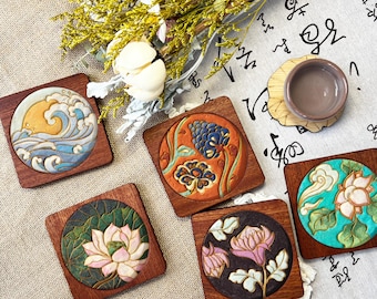 May include: A collection of five square wooden coasters with embossed floral and wave designs. Each coaster features a different design in shades of blue, orange, green, and pink. A small teacup sits on a bamboo coaster.