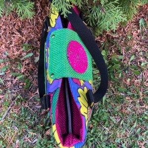 Puede incluir: Una bolsa de mano colorida con un estampado floral verde, rosa y amarillo. La bolsa tiene una correa negra y una cremallera.