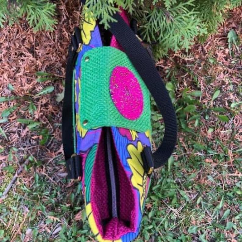 Puede incluir: Una bolsa de mano colorida con un estampado floral verde, rosa y amarillo. La bolsa tiene una correa negra y una cremallera.