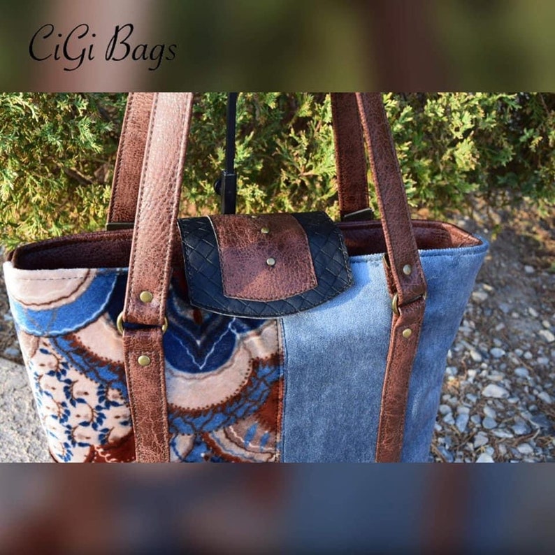 Puede incluir: Un bolso tote de cuero marr&oacute;n con un panel de tela estampado en azul y blanco y una solapa de cuero marr&oacute;n con un detalle tejido negro. El bolso tiene dos asas de cuero marr&oacute;n y detalles met&aacute;licos dorados.