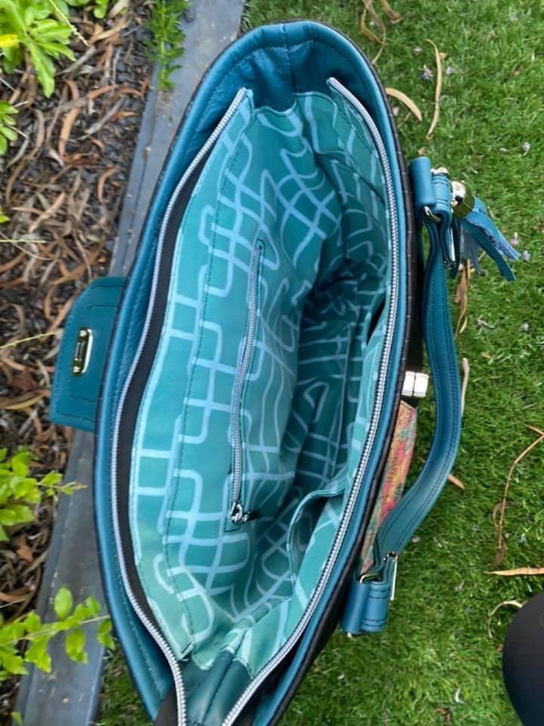 Puede incluir: Un bolso tote azul turquesa con una cremallera negra y un forro estampado en blanco y negro. El bolso tiene un asa superior y una correa para el hombro.