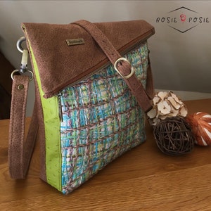 Peut inclure: Un sac à bandoulière en cuir marron avec une fermeture éclair verte et une bandoulière verte. Le sac a un rabat qui se replie et est sécurisé par une boucle en métal. Le sac est fait d'un tissu tissé avec un motif coloré. Le sac est fait main.