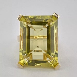 May include: A gold ring with a large, emerald-cut, light green gemstone.
