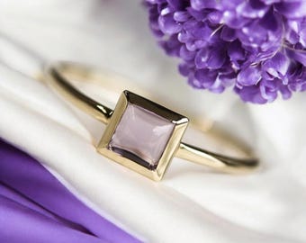 May include: A gold ring with a square-shaped, light purple gemstone.