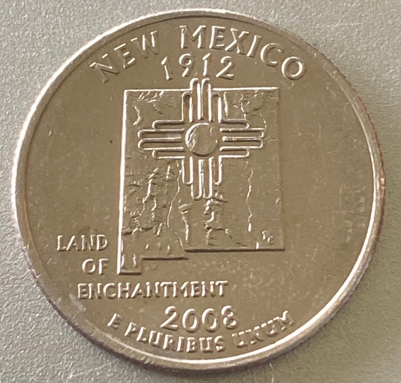 Puede incluir: Una moneda de veinticinco centavos de d&oacute;lar estadounidense con el dise&ntilde;o del estado de Nuevo M&eacute;xico. La moneda muestra las palabras "New Mexico 1912" en la parte superior, con "Land of Enchantment" y "2008" en la parte inferior. La moneda es de color plateado.