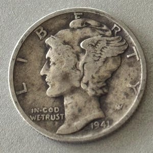 May include: A silver coin with a profile of a person wearing a winged cap, with the text "LIBERTY" and "IN GOD WE TRUST". The year "1941" is visible. The coin has a worn, aged appearance.