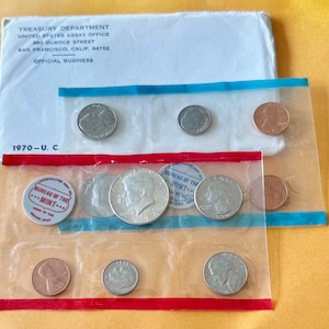 May include: A collection of United States coins in clear plastic packaging. The packaging includes a white envelope with text from the Treasury Department and the year 1970. The coins include a half dollar, quarter, dime, and penny.
