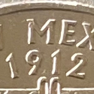 Puede incluir: Primer plano de una moneda de plata con la inscripci&oacute;n "NEW MEXICO 1912". El texto est&aacute; en relieve sobre la superficie de la moneda. El dise&ntilde;o de la moneda presenta una vista parcial del nombre del estado y el a&ntilde;o de su admisi&oacute;n.