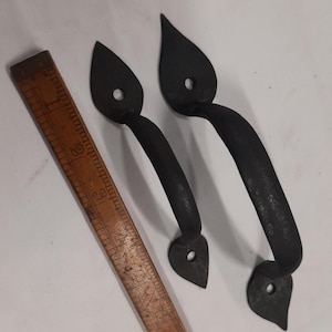 May include: Two black metal door pulls with a leaf-shaped design. The pulls are approximately 13 cm long and have a hole in the centre of each leaf.
