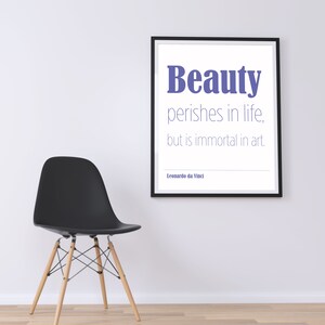 Puede incluir: Una impresión enmarcada en negro con fondo blanco y una cita en texto morado que dice "La belleza perece en la vida, pero es inmortal en el arte." La cita se atribuye a Leonardo da Vinci. Una silla negra con patas de madera está en primer plano.