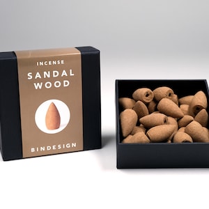 Op de afbeelding: Een zwarte doos met de tekst "INCENSE SANDAL WOOD" en het logo "BINDESIGN". De doos bevat bruine wierookkegels.