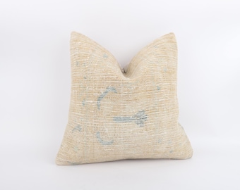 May include: A beige cushion with a textured surface and light blue details. The rectangular cushion is set against a white backdrop. The design features a subtle, faded pattern. The cushion is suitable for a sofa or bed.