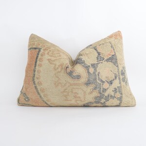 May include: Rectangular cushion with a vintage design. The cushion has a beige background with a floral pattern in peach and navy blue. The edges have a peach border. The cushion is placed on a white surface.