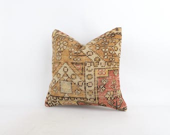 Puede incluir: Un cojín cuadrado con una funda de tejido textil que presenta un patrón geométrico multicolor en tonos beige, marrón, crema y rojo apagado. El diseño consiste en formas y líneas repetitivas complejas en toda la superficie.