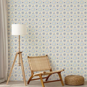 May include: A light wood chair with a woven cane seat and back sits in front of a wall covered in yellow, blue, and pink patterned wallpaper. A white lamp with a wooden tripod stand is to the left of the chair. A small woven footstool is in the foreground.