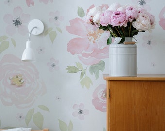 May include: A white wall with a floral wallpaper pattern featuring pink watercolour flowers. A bouquet of pink peonies in a white ceramic jug sits on a wooden cabinet.
