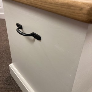May include: White wooden storage box with a natural wood top and a black metal handle. The box has a simple, farmhouse style.