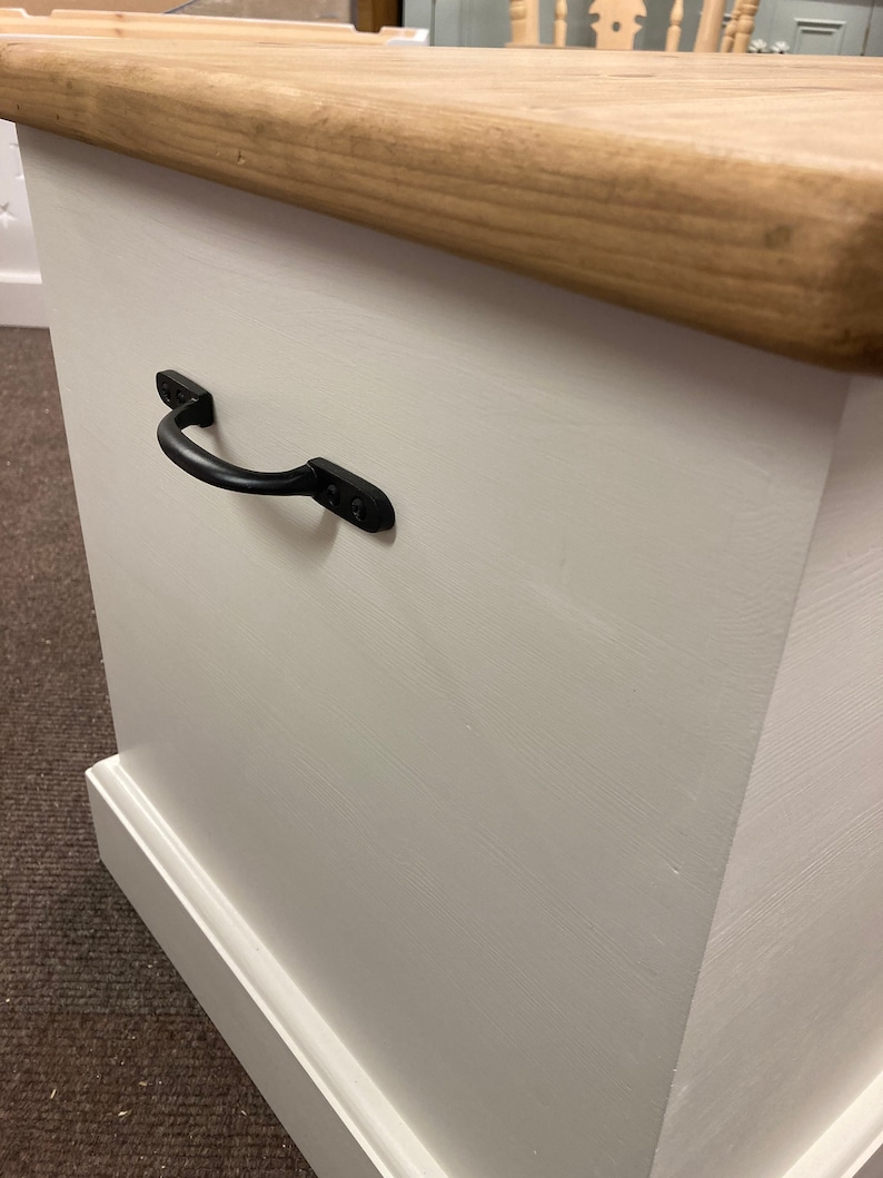May include: White wooden storage box with a natural wood top and a black metal handle. The box has a simple, farmhouse style.