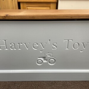 May include: A white wooden toy box with a light brown lid. The box has "Harvey's Toys" engraved on the front, along with a small tractor design.