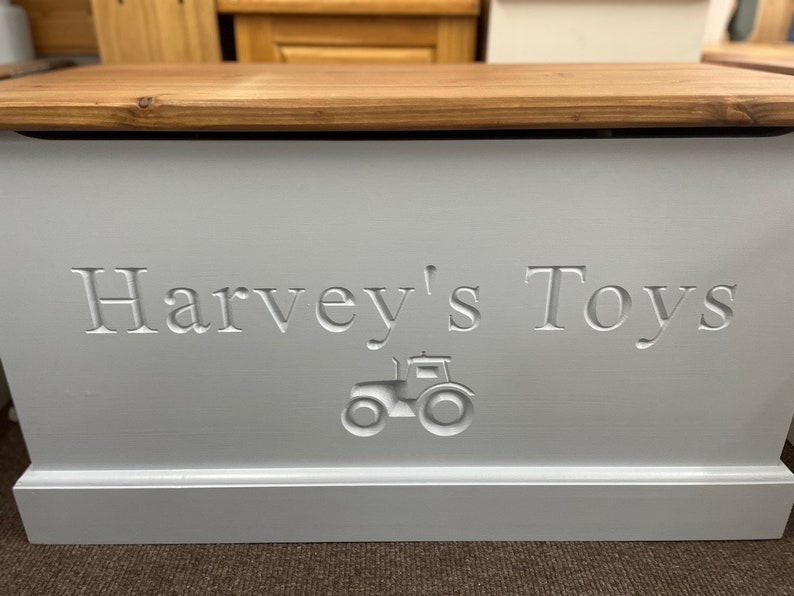 May include: A white wooden toy box with a light brown lid. The box has "Harvey's Toys" engraved on the front, along with a small tractor design.