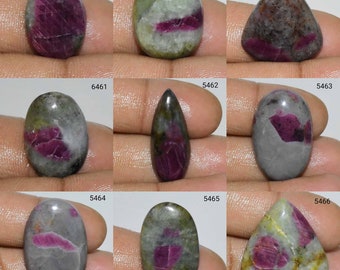 Puede incluir: Nueve piedras preciosas talladas en cabujón con una variedad de formas y colores, incluyendo oval, pera y triángulo. Las piedras son una mezcla de gris, verde y rosa con inclusiones rojas. Las piedras están etiquetadas con los números 5458, 5459, 5460, 6461, 5462, 5463, 5464, 5465 y 5466.