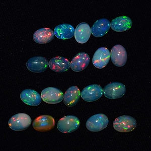 May include: A collection of 17 oval-shaped opals with a variety of iridescent colours, including blue, green, red, and orange. The opals are arranged in rows on a black background.
