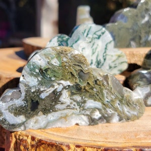 May include: A green and white agate stone carved into a cloud shape. The stone has a natural, organic look with swirls of green, white, and gray.