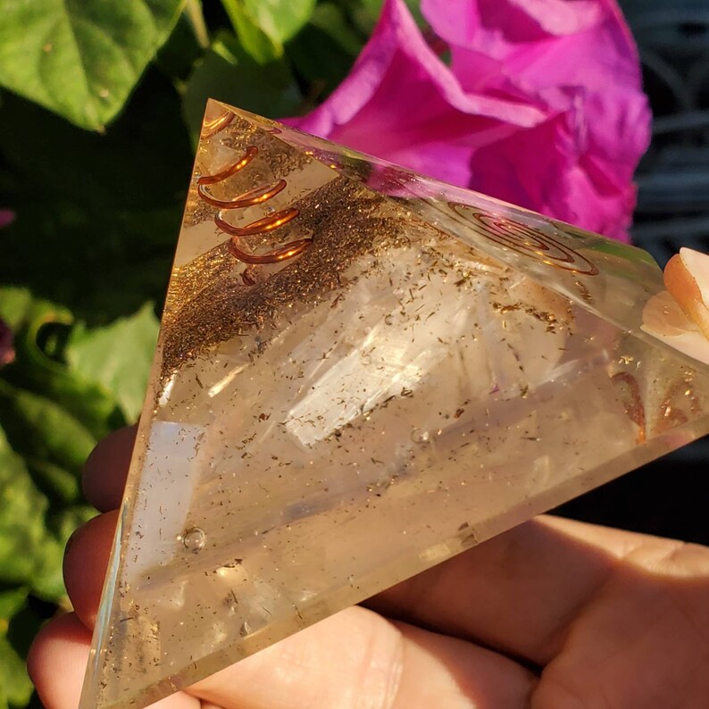 May include: A clear quartz crystal pyramid with a copper wire coil embedded inside. The pyramid is filled with small gold flecks and has a white crystal shard inside.