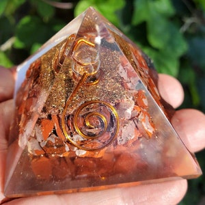 K&ouml;nnte beinhalten: Eine klare Quarzpyramide mit einem roten Jaspis- und Goldflocken-Inneren. Eine Kupferspirale ist in der Mitte der Pyramide eingebettet.