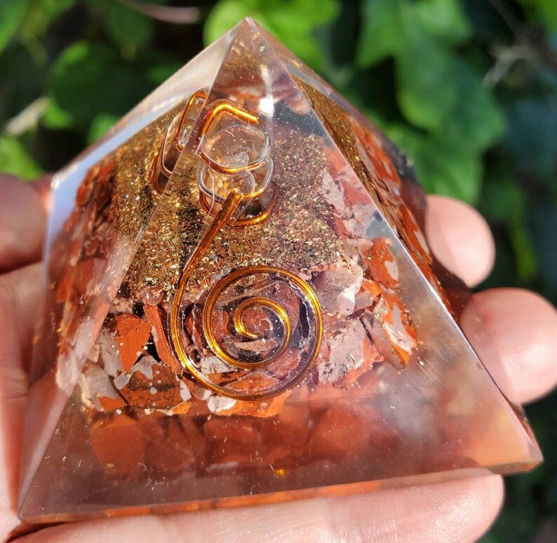 K&ouml;nnte beinhalten: Eine klare Quarzpyramide mit einem roten Jaspis- und Goldflocken-Inneren. Eine Kupferspirale ist in der Mitte der Pyramide eingebettet.