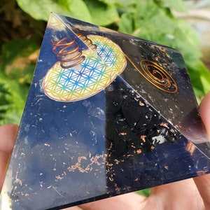 May include: Black obsidian pyramid with a copper wire coil and a flower of life design on one side. The pyramid is approximately 2 inches tall.