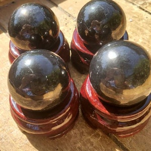 May include: Four black obsidian spheres on wooden stands. The spheres are polished and reflect light. The stands are a dark reddish brown.