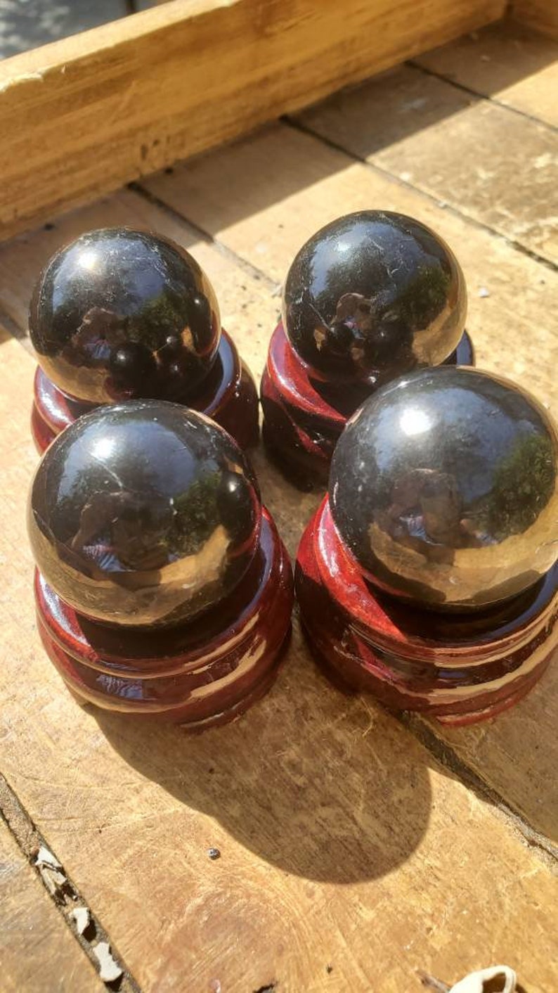 May include: Four black obsidian spheres on wooden stands. The spheres are polished and reflect light. The stands are a dark reddish brown.
