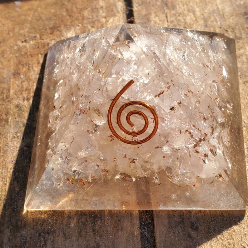 K&ouml;nnte beinhalten: Eine klare Quarzkristallpyramide mit einer Kupferspirale auf der Spitze. Die Pyramide besteht aus vielen kleinen Quarzst&uuml;cken, die miteinander verklebt sind.