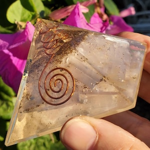 May include: A clear quartz crystal pyramid with a copper wire spiral design. The pyramid is filled with small, clear crystals and has a light brown tint.