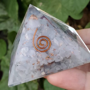 K&ouml;nnte beinhalten: Eine klare Kristallpyramide mit einer Kupferspirale im Inneren. Die Pyramide ist mit kleinen wei&szlig;en Kristallen und Kupferflocken gef&uuml;llt.
