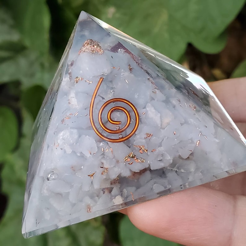 K&ouml;nnte beinhalten: Eine klare Kristallpyramide mit einer Kupferspirale im Inneren. Die Pyramide ist mit kleinen wei&szlig;en Kristallen und Kupferflocken gef&uuml;llt.