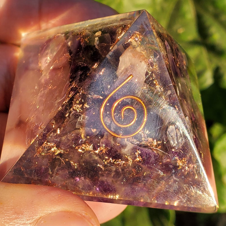 K&ouml;nnte beinhalten: Eine klare Quarzpyramide mit einer Kupferspirale im Inneren. Die Pyramide ist mit Amethystkristallen und Goldflocken gef&uuml;llt.