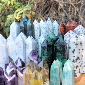 May include: A collection of various crystal points, including amethyst, citrine, green aventurine, and white calcite. The points are arranged in a semi-circle on a wooden surface.