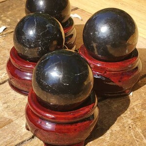 May include: Four black obsidian spheres on wooden stands. The spheres are polished and have a reflective surface. The stands are a dark red colour.
