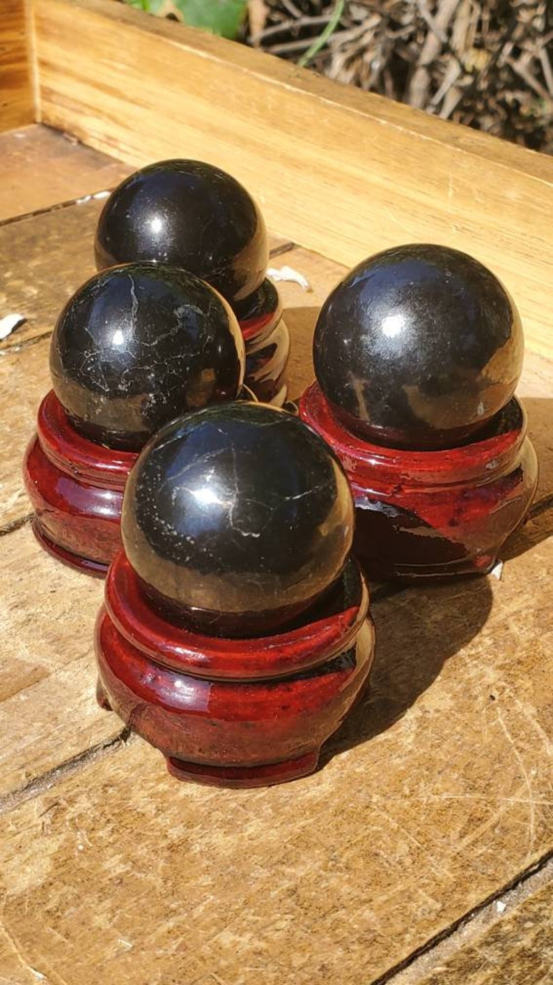 May include: Four black obsidian spheres on wooden stands. The spheres are polished and have a reflective surface. The stands are a dark red colour.