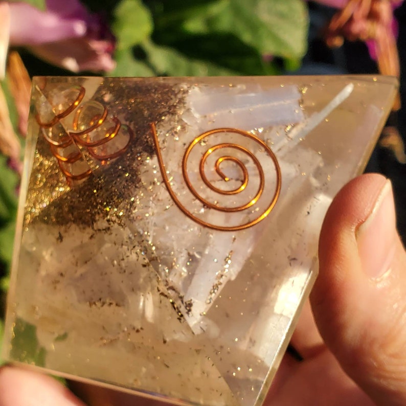 May include: A clear quartz pyramid with a copper wire spiral design. The pyramid is filled with small pieces of clear quartz and pyrite.