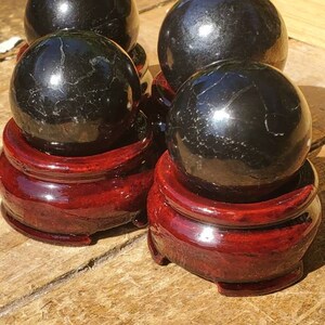 May include: Four black obsidian spheres on red wooden stands. The spheres are polished and reflect light.